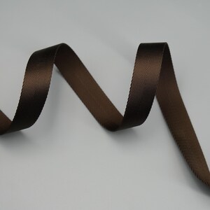 Peut inclure: Gros plan sur un ruban marron avec un motif chevron subtil. Le ruban est d'un brun riche et fonc&eacute; et semble &ecirc;tre fait d'un mat&eacute;riau durable. Le ruban est incurv&eacute; et a un l&eacute;ger &eacute;clat, sugg&eacute;rant qu'il pourrait &ecirc;tre utilis&eacute; pour divers travaux manuels ou d&eacute;coratifs.