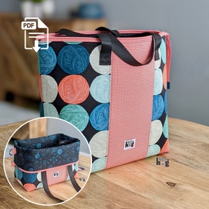 Puede incluir: Una bolsa de mano rosa y negra con un patrón de ovillos de lana y el texto "Reda Hug" en el lateral. La bolsa tiene una cremallera negra y asas negras. Una bolsa de mano más pequeña de color negro y rosa con un patrón en blanco y negro está en primer plano.