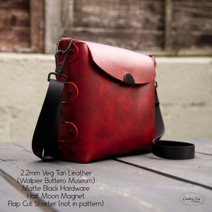 May include: A red leather crossbody bag with a black strap and black hardware. The bag has a flap closure with a half-moon magnet. The bag is made of 2.2mm veg tan leather from the Walpier Buttero Museum. "Flap Cut Shorter (not in pattern)" is written on the bottom of the image.