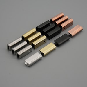 Peut inclure: Assortiment de pièces de quincaillerie métalliques dans différentes finitions, notamment argent, or, noir et cuivre. Les pièces sont rectangulaires avec un dessus et un dessous incurvés.