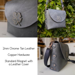 May include: A gray leather crossbody bag with a copper clasp and a leaf design. The bag has a magnetic closure and a black adjustable strap. 2mm Chrome Tan Leather Copper Hardware Standard Magnet with a Leather Cover.