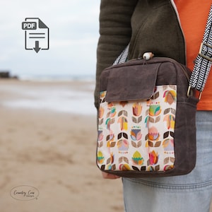 May include: A brown canvas crossbody bag with a floral print. The bag has a flap closure and a zippered pocket on the front. The bag is worn by a person on their shoulder.