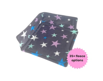 May include: A square, dark grey fleece pet bed with raised sides, featuring a repeating pattern of white, light blue, and lavender stars. A pink circular badge on the side displays the text 35+ fleece options.
