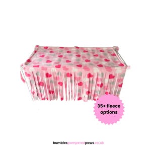 May include: A rectangular fleece hammock featuring a repeating pattern of pink, red, and white hearts. The fabric has a fringed edge along the bottom and includes a pink star-shaped graphic with the text 35+ fleece options and the URL bumblespamperedpaws.co.uk.