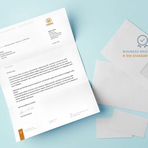 Pu&ograve; includere: Un set di cancelleria aziendale su una superficie azzurra. Il set comprende una carta intestata con testo e logo, una busta bianca con la scritta "BUSINESS BRIEF # DIN STANDARD" e due biglietti da visita vuoti.