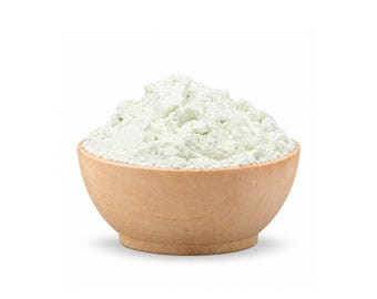 May include: A small, round, light-colored wooden bowl filled to the brim with a mound of fine, pale green powder. The texture of the powder appears soft and powdery, forming a rounded peak that rises slightly above the rim of the wooden container.
