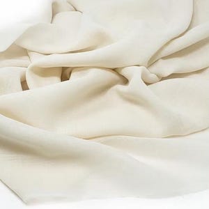 May include: A close-up of a white fabric, showing its soft and smooth texture. The fabric is draped and folded, highlighting its flowy and delicate nature.