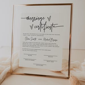 Peut inclure: Un certificat de mariage encadré avec une calligraphie élégante. Le texte indique « certificat de mariage » avec les noms Olivia Smith et Michael Brown. Le certificat comprend des espaces pour les signatures et est encadré d'or.