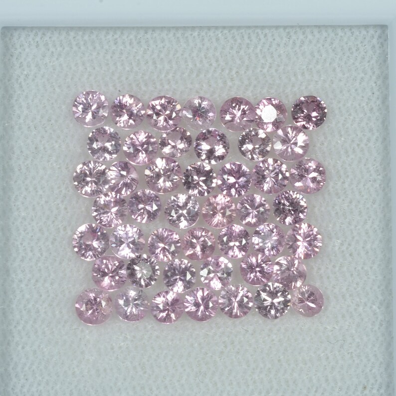May include: A collection of round, light pink gemstones arranged in a square formation. Each gem has multiple facets, reflecting light. The gems are set against a white background, creating a clean and elegant presentation.