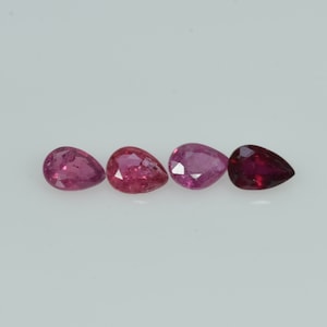 May include: Four pear-shaped gemstones in shades of red and pink are displayed. The gems vary in colour, from light pink to deep ruby red, with facets visible on some. The stones are set against a plain white background.