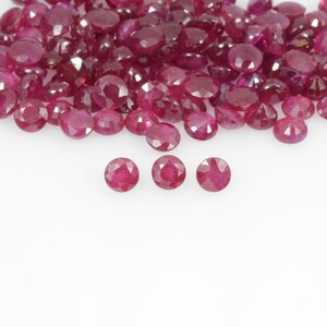 Peut inclure: Une collection de pierres précieuses rubis rondes et facettées de différentes tailles. Les pierres précieuses sont d'un rouge profond et sont dispersées sur une surface blanche. Trois rubis sont mis au point en bas de l'image.