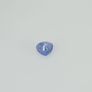 May include: A faceted, heart-shaped, blue gemstone. The gem has a light blue hue with subtle variations in color. The facets catch the light, creating a sparkling effect. The gemstone is set against a plain white background.