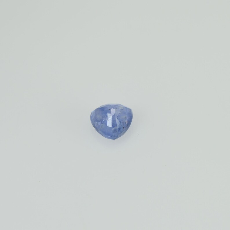 May include: A faceted, heart-shaped, blue gemstone. The gem has a light blue hue with subtle variations in color. The facets catch the light, creating a sparkling effect. The gemstone is set against a plain white background.