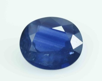 May include: A deep blue, oval-cut gemstone with multiple facets. The polished surface reflects light, creating a brilliant appearance. The colour is a rich, saturated blue, with slight tonal variations across the surface. A gemstone suitable for jewellery.