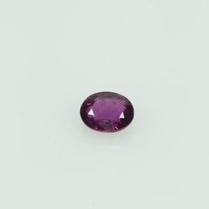 May include: An oval-shaped, faceted gemstone with a deep magenta hue. The gem is set against a white background, showcasing its clarity and brilliance. The cut of the stone reveals multiple facets, enhancing its sparkle.
