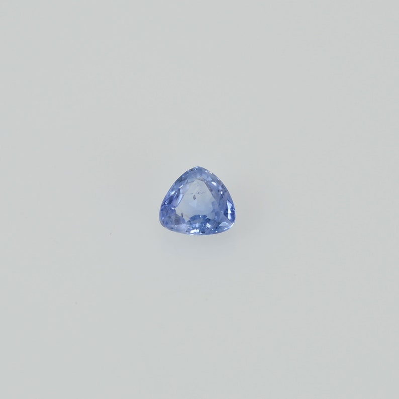 May include: A light blue, triangular gemstone with a polished surface. The gem is set against a white background, showcasing its clarity and color. The shape is a perfect equilateral triangle, ideal for jewelry.