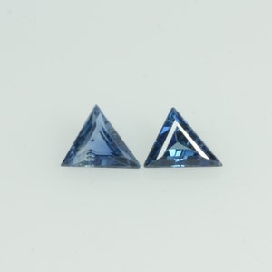Puede incluir: Dos gemas triangulares facetadas en tonos azules. Las gemas se colocan sobre un fondo blanco, mostrando su forma geométrica y color. Las facetas crean un juego de luces y sombras.