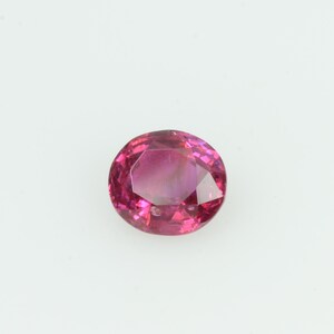 May include: A faceted, oval-shaped gemstone in a vibrant shade of pink. The gem has a polished surface with multiple facets that reflect light, creating a sparkling effect. The gemstone is set against a plain white background.