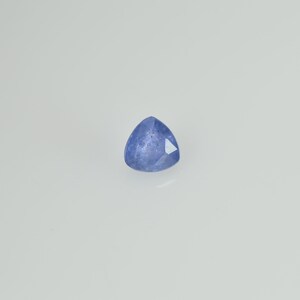 May include: A faceted, triangular blue gemstone. The gem has a light blue hue with a polished surface and sharp edges. The gemstone is set against a white background, highlighting its color and shape.