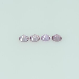 May include: Four round, faceted gemstones in a row. The gems are a light purple color and appear to be cut with many facets. The background is a solid, light-colored surface.