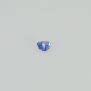 May include: A faceted, triangular blue gemstone. The gem has a light blue hue with a slightly darker blue at the edges. The stone is set against a plain white background.