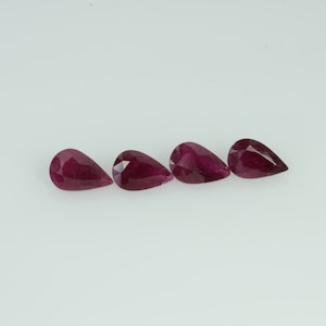 Peut inclure: Quatre rubis en forme de poire, facettés, sont présentés sur un fond blanc. Les pierres précieuses sont d'un rouge profond et riche, avec des facettes visibles qui captent la lumière. Les rubis sont disposés en ligne horizontale.