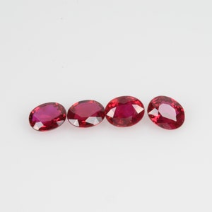 May include: Four oval-cut, deep red gemstones are displayed against a white backdrop. The gems have a polished, reflective surface, highlighting their rich colour and internal structure. These gemstones could be used for jewellery.