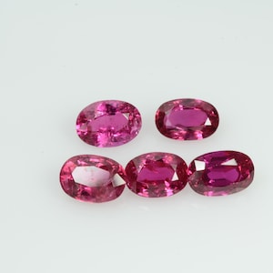 May include: Five oval-cut, vibrant pink gemstones are displayed against a white background. The gems have a faceted surface, catching the light and showcasing their rich color. These gemstones are likely rubies or pink sapphires.