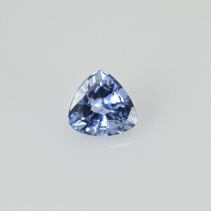 Puede incluir: Una gema triangular de color azul claro con una superficie facetada. La gema se encuentra sobre un fondo blanco, mostrando su claridad y color. La forma es un triángulo equilátero perfecto, que refleja la luz.