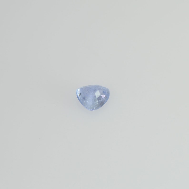 May include: A light blue, heart-shaped gemstone with a faceted surface. The gem is set against a plain white background, highlighting its color and shape. The facets catch the light, creating a sparkling effect.