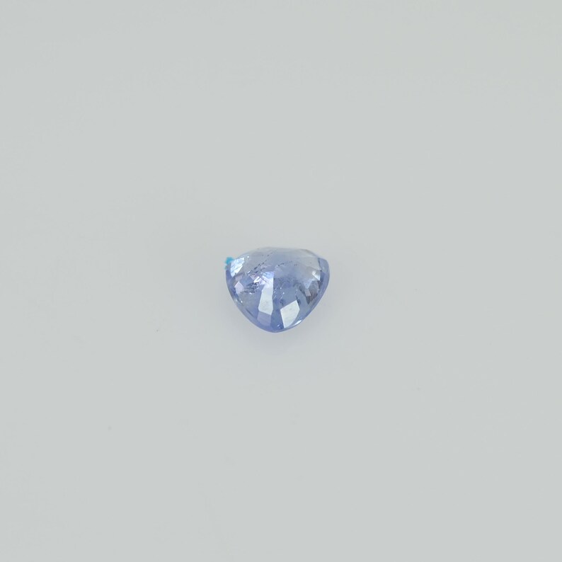 May include: A light blue, heart-shaped gemstone with a faceted surface. The gem is set against a plain white background, highlighting its color and shape. The gemstone is likely a sapphire or similar precious stone.