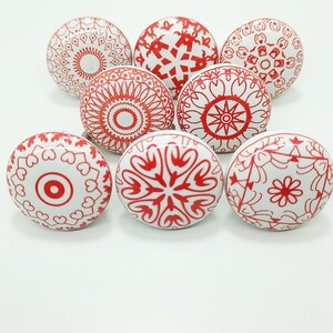 May include: Eight white ceramic cabinet knobs with red decorative patterns. The designs include floral, geometric, and mandala-style motifs. These decorative knobs are ideal for adding a unique touch to furniture.