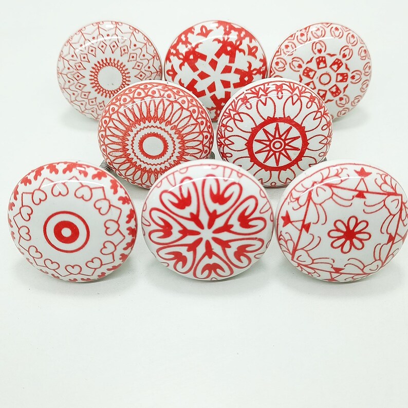 May include: Eight white ceramic cabinet knobs with red decorative patterns. The designs include floral, geometric, and mandala-style motifs. These decorative knobs are ideal for adding a unique touch to furniture.