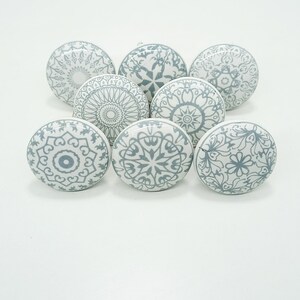 May include: Eight white ceramic cabinet knobs with detailed grey floral and geometric designs. The knobs are round and have a glossy finish, ideal for adding a decorative touch to furniture or cabinets. Each knob has a diameter of approximately 4 cm.