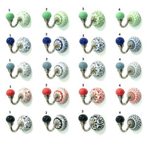 Op de afbeelding: Een collectie van twintig wandhaken gerangschikt in een raster, elk voorzien van een zilverkleurige J-vormige metalen haak en een ronde keramische basis. De basissen tonen diverse ingewikkelde patronen in groen, blauw, lichtblauw, rood en zwart.