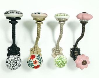 May include: Four decorative wall hooks with ceramic knobs. The hooks have different designs, including floral and geometric patterns, and a variety of colors such as black, white, pink, green, and gold. The hooks are made of metal.