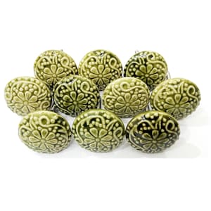 May include: A collection of eleven olive green ceramic cabinet knobs. Each knob features a raised floral design with a glossy finish. The knobs are arranged on a white background, showcasing their decorative details.