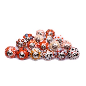 May include: A collection of decorative ceramic cabinet knobs in various colors and patterns. The knobs feature floral, geometric, and dotted designs in shades of orange, white, blue, and yellow. Each knob has a silver metal base.