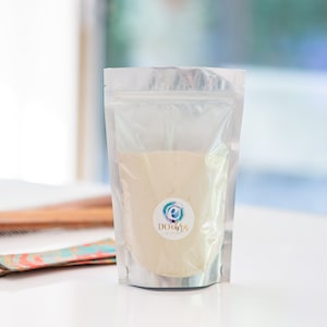 May include: A silver stand-up pouch with a white label that says "DOCHIRA" in a blue and green circle. The pouch contains a beige powder.