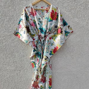 May include: A white cotton kaftan with a floral print in shades of red, pink, blue, green, and yellow. The kaftan has a V-neck and a tie at the waist.