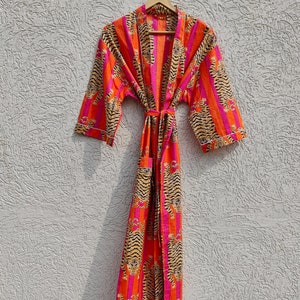 May include: A long, orange and pink striped robe with a tiger print. The robe has a tie belt and is hanging on a hanger.