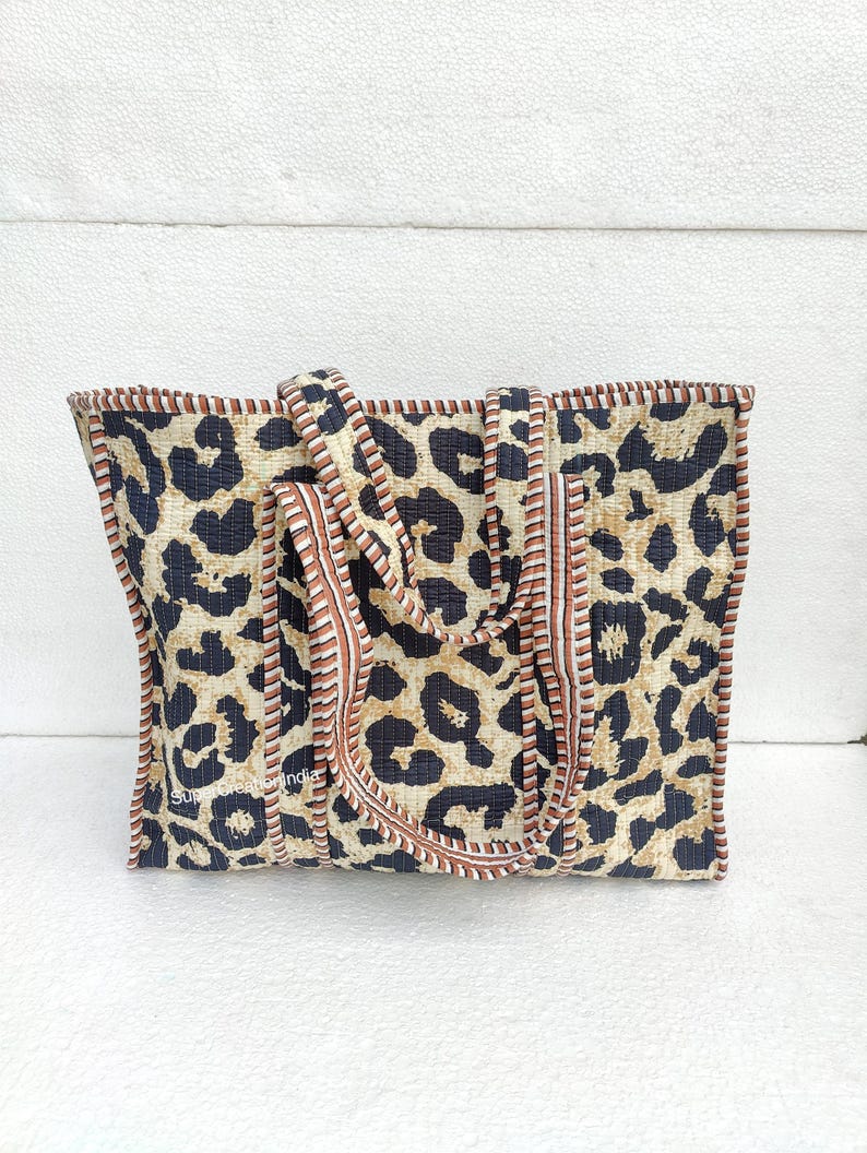 May include: A large tote bag with a leopard print design. The bag has brown and white stripes along the top edge and brown straps.