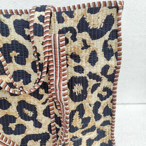 May include: A large tote bag with a leopard print design. The bag has brown and white striped straps and a black quilted lining. The bag is made of cotton and is perfect for carrying everyday essentials.