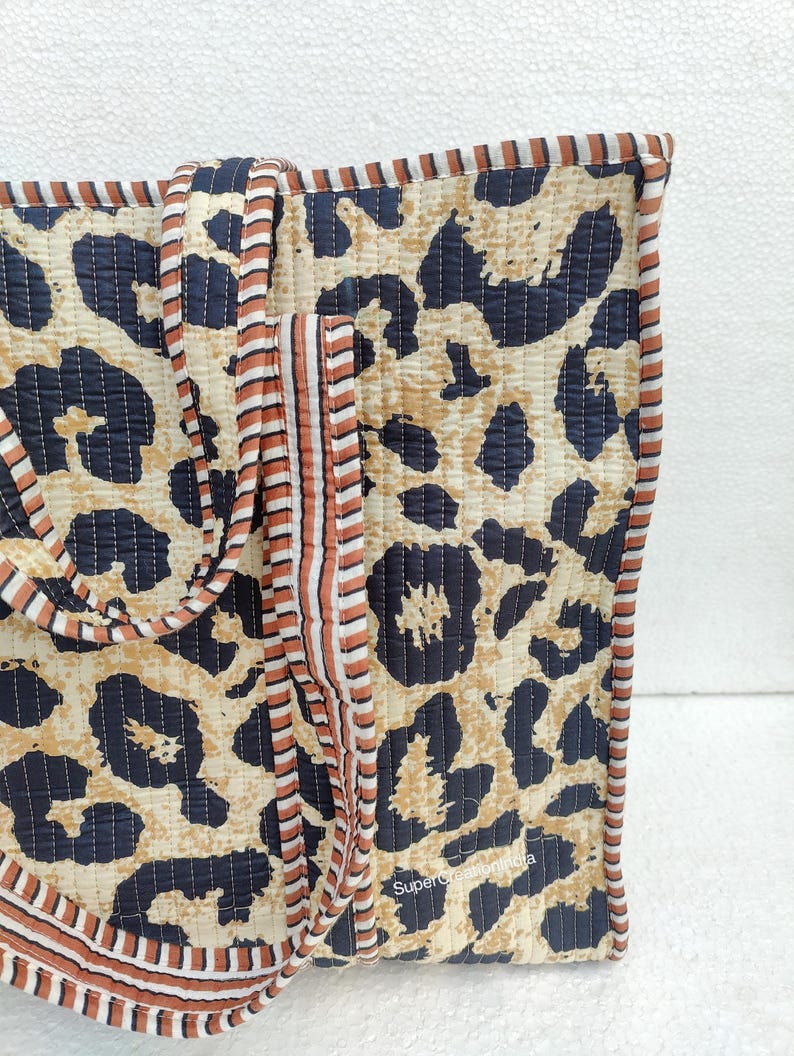 May include: A large tote bag with a leopard print design. The bag has brown and white striped straps and a black quilted lining. The bag is made of cotton and is perfect for carrying everyday essentials.