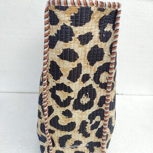 May include: A brown and black tote bag with a leopard print design. The bag has a brown and white striped trim around the edges. The bag is made of quilted fabric.