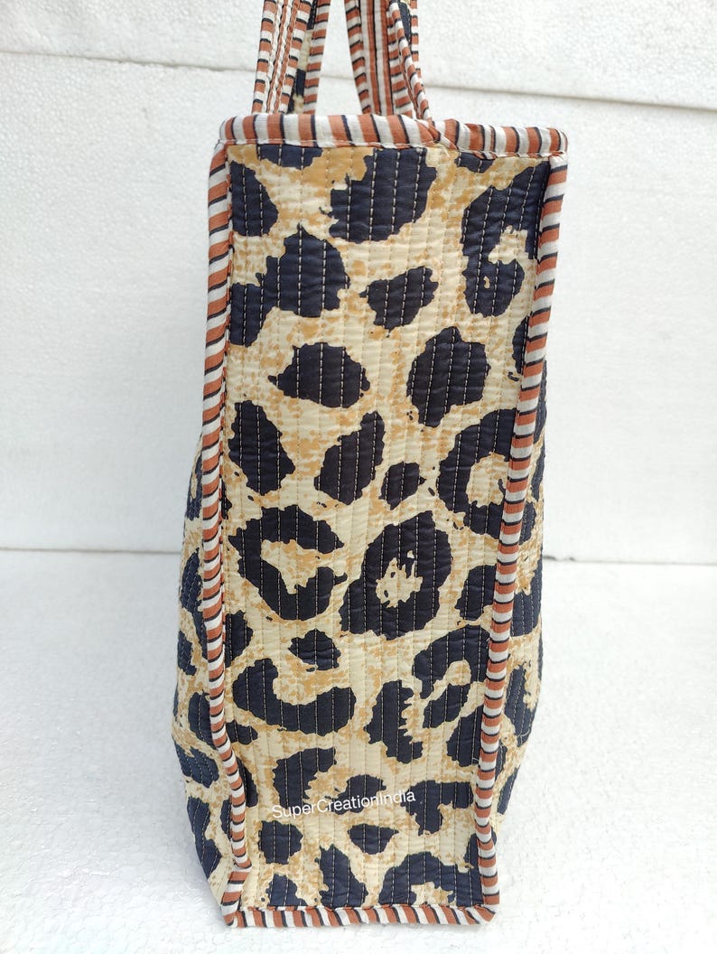 May include: A brown and black tote bag with a leopard print design. The bag has a brown and white striped trim around the edges. The bag is made of quilted fabric.