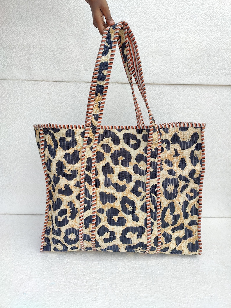 May include: A large tote bag with a leopard print design. The bag has black, brown, and white stripes around the edges and handles.