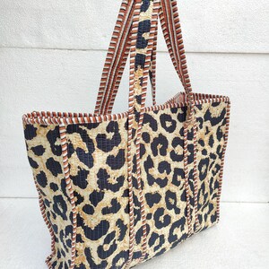 May include: A large tote bag with a leopard print design. The bag has brown and white striped straps and a brown and white trim around the edges.