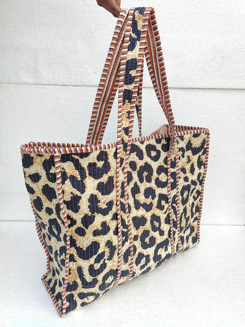 May include: A large tote bag with a leopard print design. The bag has brown and white striped straps and a brown and white trim around the edges.