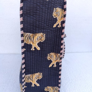 May include: A black quilted tote bag with a pink and white striped trim. The bag features a repeating pattern of orange tigers on a black background.